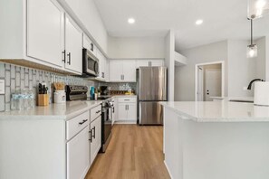 A modern kitchen with white cabinetry, stainless steel appliances, and a wooden floor. - Casa de Palmera | Team Joseph Ellen (Palm Coast)