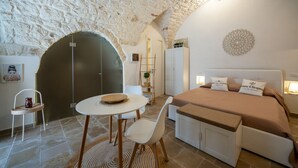 Un dormitorio acogedor con techo de piedra, cama con almohadas, mesita de noche y una pequeña zona de estar con una silla y una mesa.