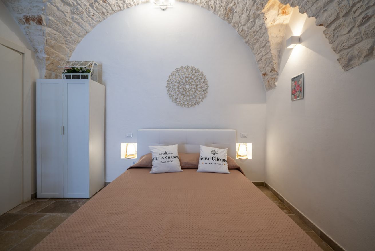 Ein Schlafzimmer mit Steinbogen-Decke, einem Bett mit zwei Kissen, einem Kleiderschrank und Wandleuchten.
