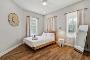Ein Schlafzimmer mit einem Bett, einer runden Wanddekoration, einem Nachttisch, einem Spiegel und einem Fenster mit Vorhängen.