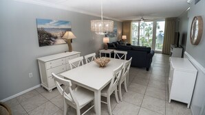 Una sala moderna con un sofá oscuro, una mesa de comedor blanca con sillas y una araña.