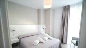 A modern hotel room with a large bed, a bedside table, a chair, and a window with curtains. - La Inmaculada Alojamientos (Málaga)