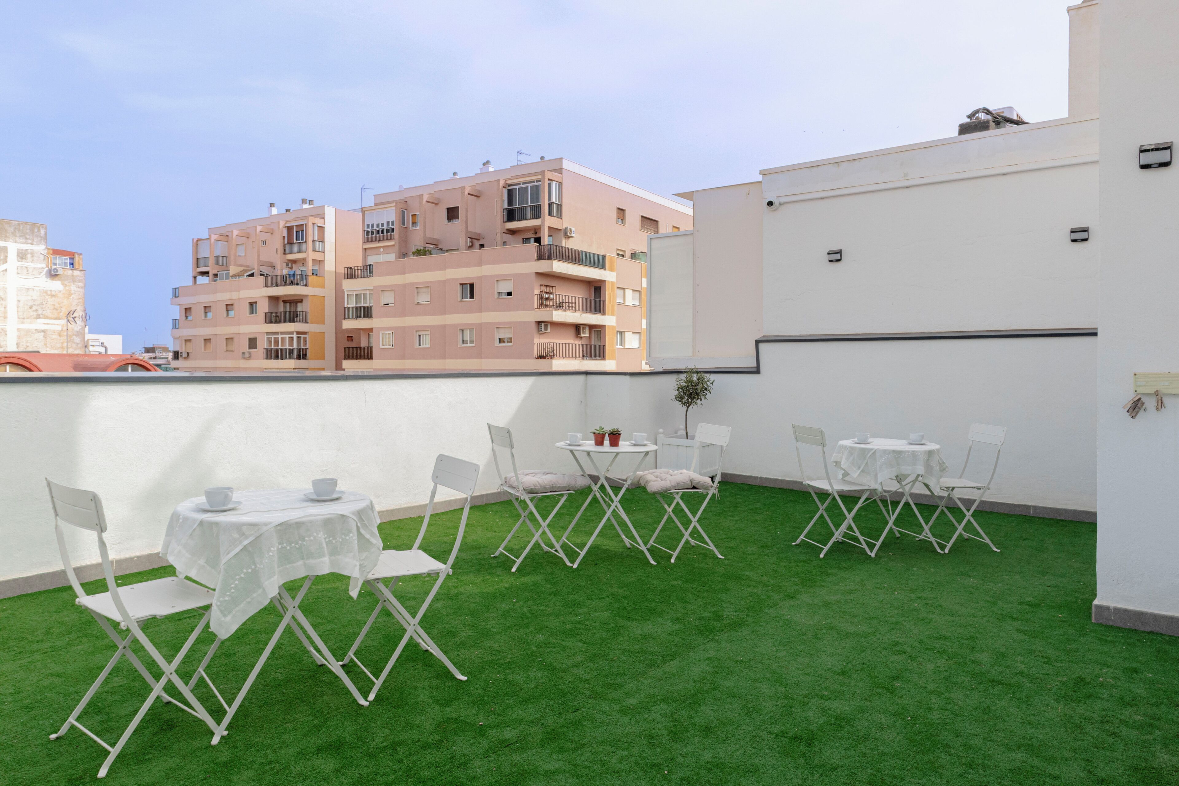 Une terrasse sur le toit, avec un revêtement de gazon synthétique, des chaises pliantes blanches, une petite table ronde et un pot de fleurs.