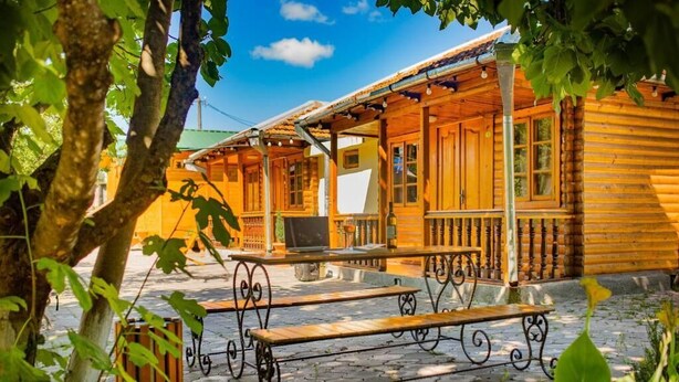 A wooden cabin with a covered porch, outdoor seating, and a stone-paved patio. - Eco cottages (Tsqaltubo)