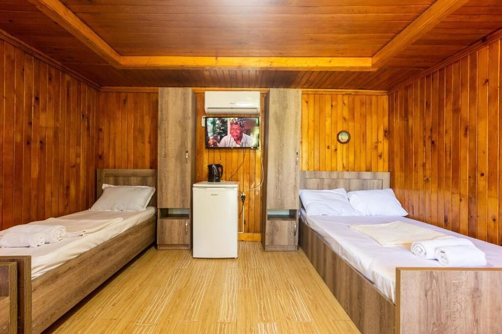 A wooden cabin room with two beds, a small refrigerator, and a television mounted on the wall.