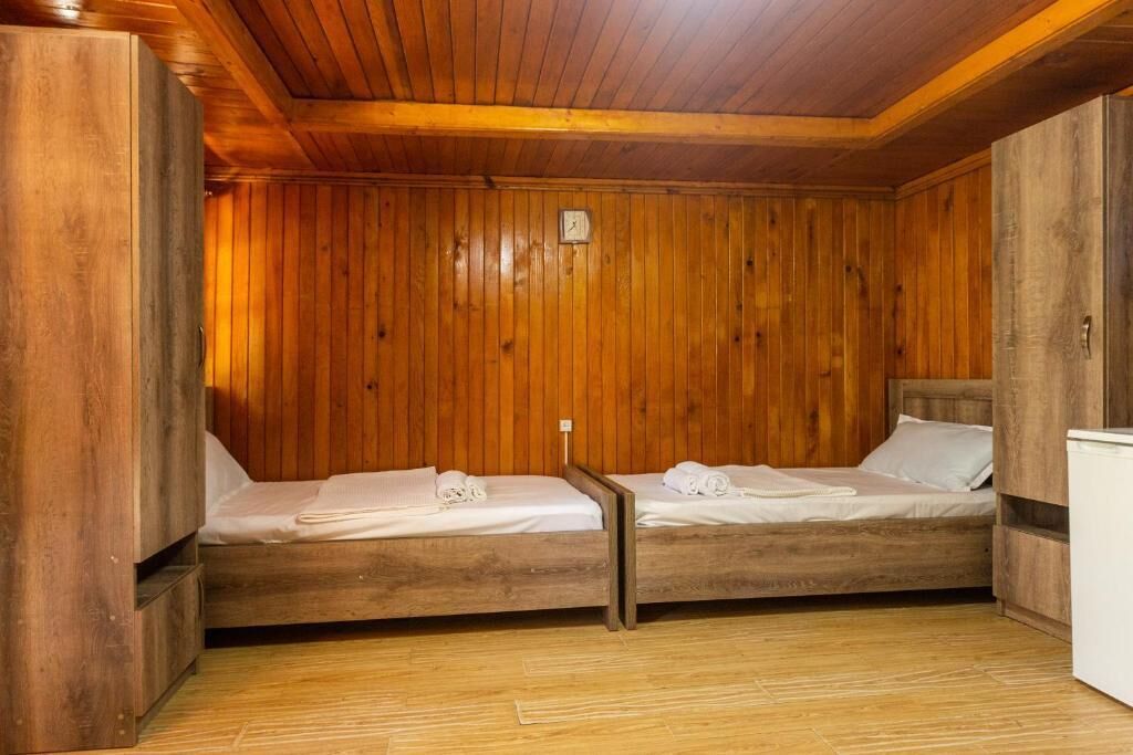 A wooden cabin room with two beds, a small table, and a white cabinet.