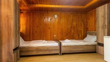 A wooden cabin room with two beds, a small table, and a white cabinet.