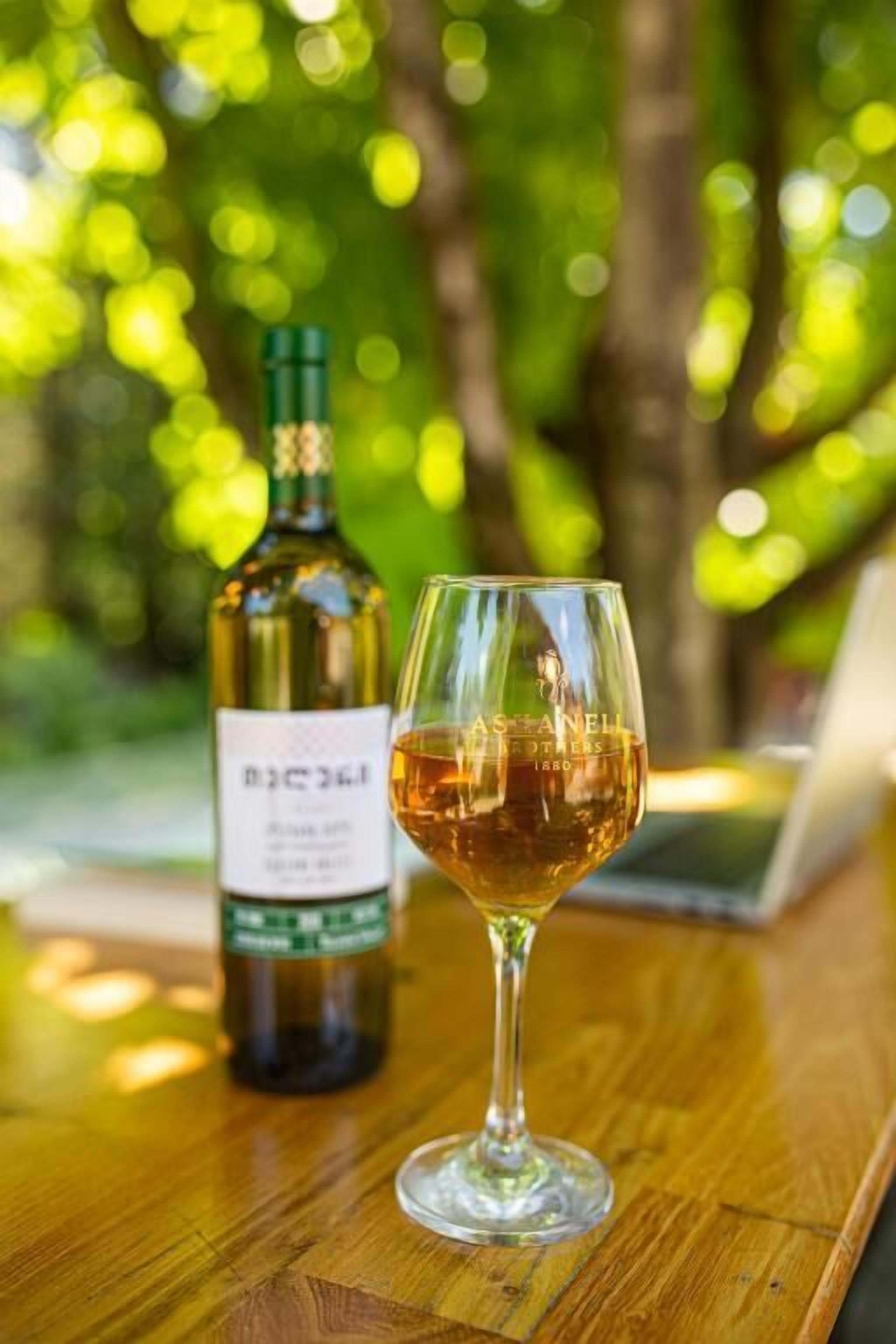 A bottle of wine and a glass on a wooden table with a blurred green background.