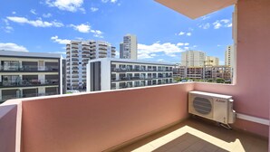 A balcony with a view of modern buildings, a Mitsubishi air conditioning unit, and a tiled floor.