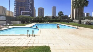 A swimming pool with two diving boards, surrounded by a tiled deck and grass.