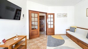 A living room with a sofa, a TV mounted on the wall, a wooden table, and a door leading to another room.