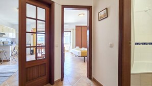 A hallway with a wooden door leading to a kitchen and a bedroom.