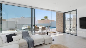 Un salon moderne avec un canapé blanc, un coin repas comprenant une table et des chaises, et une vue sur une piscine et des immeubles.