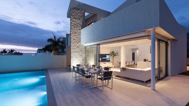 Une maison moderne dotée d’une piscine, d’un espace repas extérieur et d’une grande porte vitrée donnant sur un espace de vie.