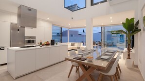 Une cuisine moderne dotée d’un îlot central, d’appareils électroménagers en acier inoxydable et d’un coin repas avec une table et des chaises en verre.