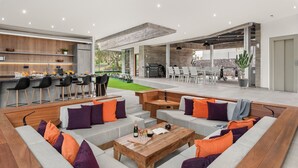 A modern outdoor living area with a bar, seating, and a view of the garden. - Villa Origen Exclusive (Adeje)