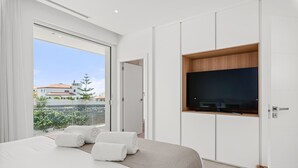 Una camera da letto moderna con un letto grande, una TV fissata al muro e un balcone con vista sul quartiere.