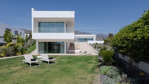 Una moderna casa a due piani con tetto piatto, ampie vetrate e un prato curato con due poltrone da relax.