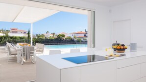Una cucina moderna con un'ampia finestra, un'area pranzo con posti a sedere esterni e vista su una piscina e case.