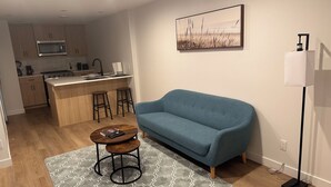 Una sala moderna con un sofá azul, una mesa de centro y una cocina al fondo.