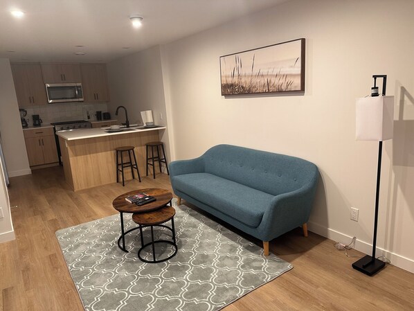 Una sala moderna con un sofá azul, una mesa de centro y una cocina al fondo.