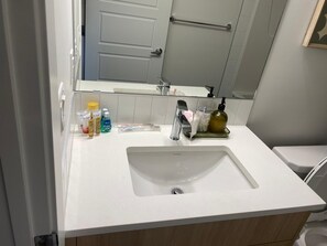Un baño con lavamanos blanco, espejo y artículos de tocador sobre la encimera.