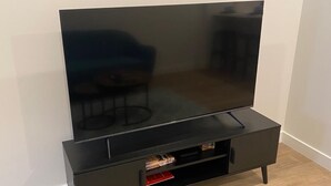 Un mueble multimedia negro con un televisor de pantalla plana, un cajón y un estante con libros.