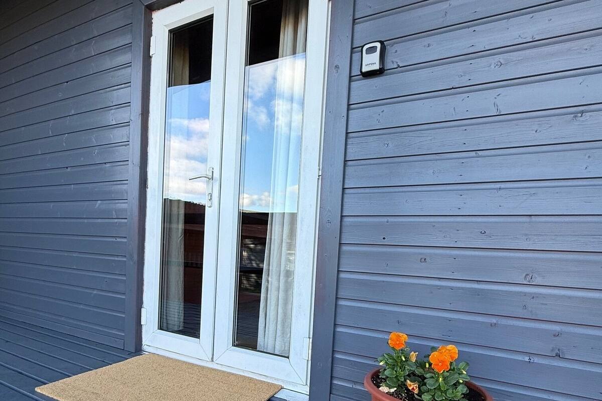 Une maison à l’extérieur gris, avec une porte à cadre blanc et un paillasson marron.