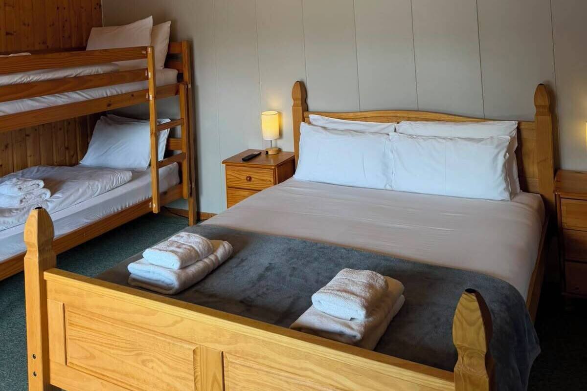 Une chambre avec un lit superposé en bois, un lit simple, une table de chevet et un ventilateur de plafond.