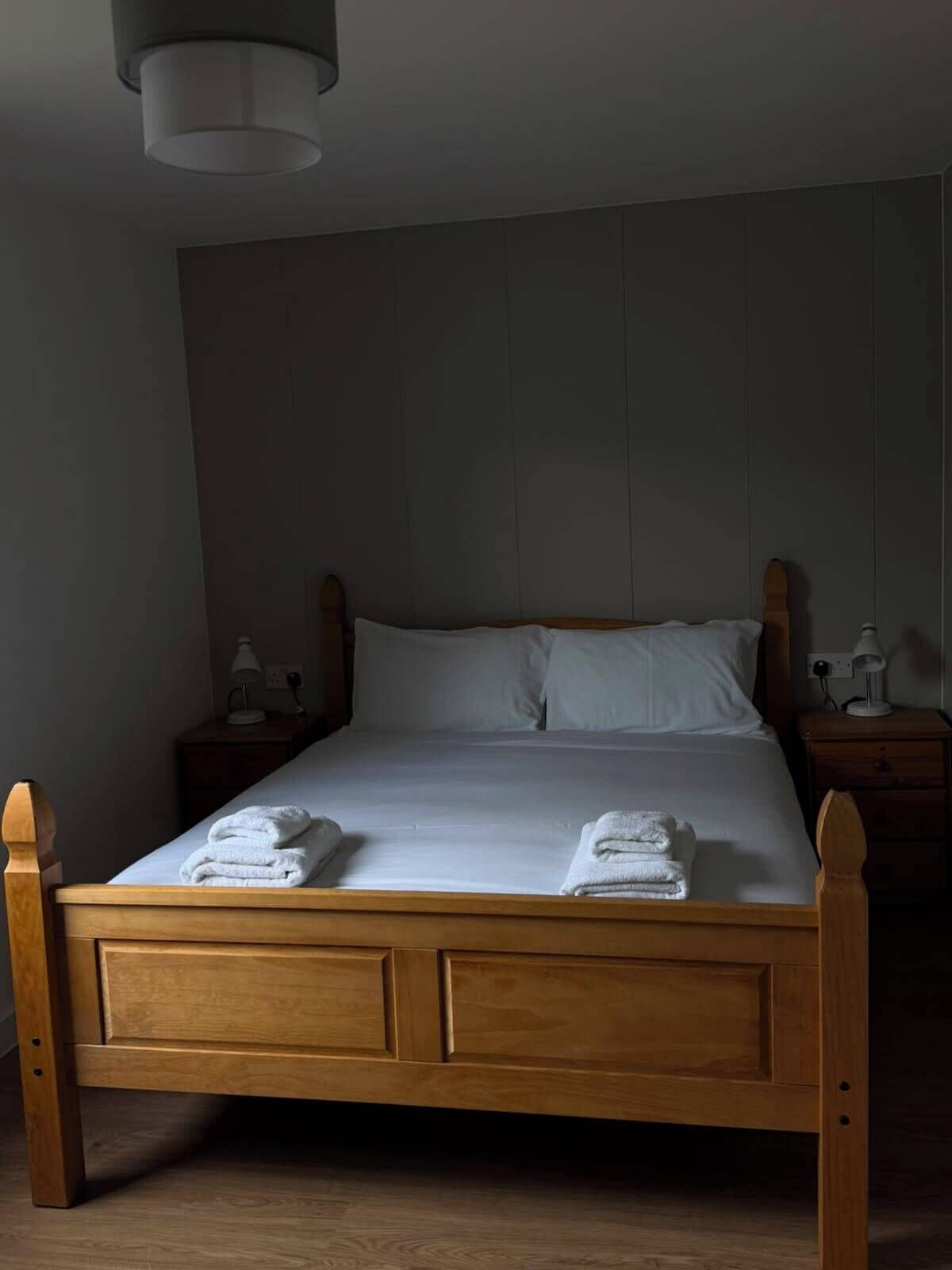 A wooden bed with white linens, two bedside tables, and a wall-mounted light fixture.