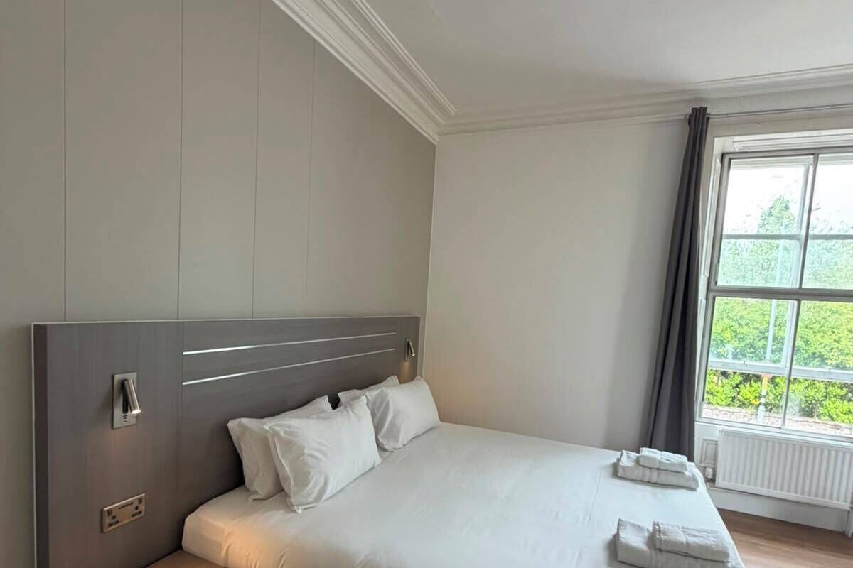 Une chambre d’hôtel moderne dotée d’un grand lit, de tables de chevet, d’une fenêtre offrant une vue agréable et d’un radiateur intégré.
