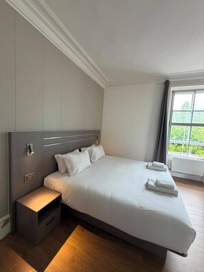 A modern hotel room with a large bed, bedside tables, a window with a view, and a built-in heater. - Ox Hotel Spean Bridge (Spean Bridge)