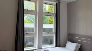 Een slaapkamer met een bed, een stoel, een bureau en een raam met gordijnen.
