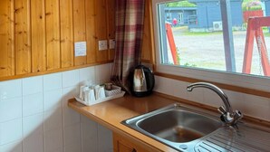 Een houten interieur met een raam, een wastafel, een waterkoker en een ruitjesgordijn.