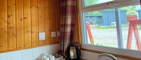 A wooden interior with a window, a sink, a kettle, and a plaid curtain.