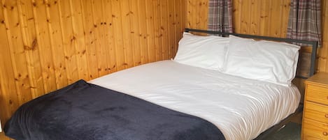 A wooden-paneled room with a bed, a nightstand, and a window with curtains.
