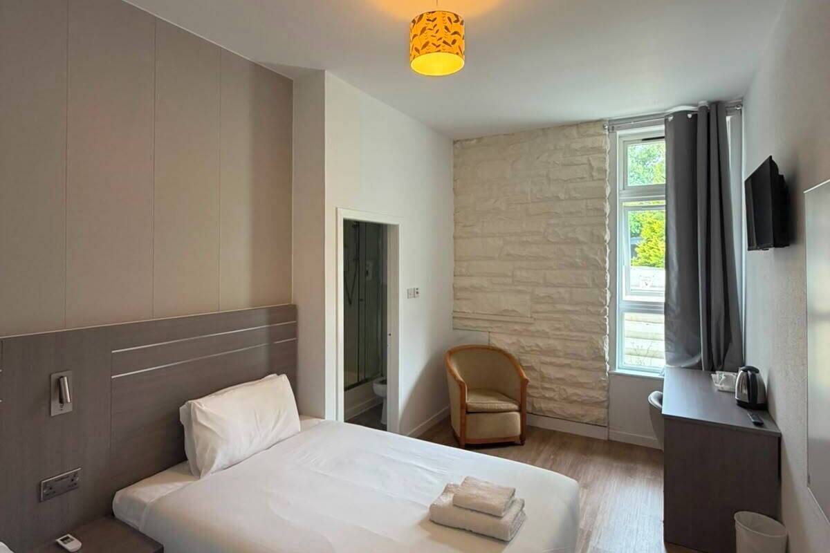 Une chambre d’hôtel équipée d’un lit, d’une table de chevet, d’une chaise et d’un téléviseur fixé au mur.