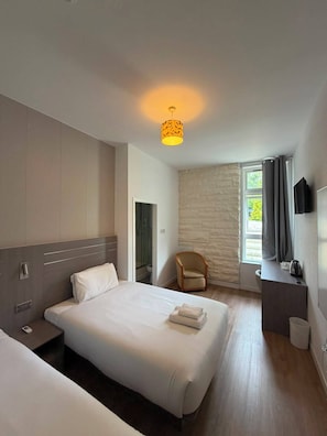 Une chambre d’hôtel équipée d’un lit, d’une table de chevet, d’une chaise et d’un téléviseur fixé au mur.