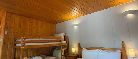 Habitación con literas de madera, una cama individual, mesitas de noche y una pequeña mesa.