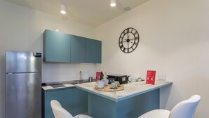 A compact kitchen with teal cabinets, a stainless steel refrigerator, a microwave, and a clock on the wall. There are two white chairs and a small island with a woven placemat. - Waterfront Dream by Wonderful Italy (Genova)