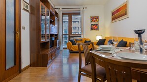 A cozy living room with a wooden bookshelf, a yellow sofa, and a dining table set for two. - Adriano Apartment by Wonderful Italy (Torino)