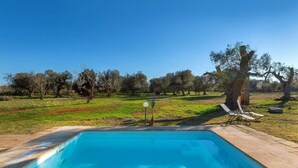Une piscine rectangulaire avec une terrasse carrelée, entourée d’une pelouse agrémentée d’arbres et sous un ciel dégagé.