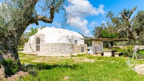Une maison blanche, en forme de dôme, avec des murs en pierre, entourée de verdure et d’arbres.