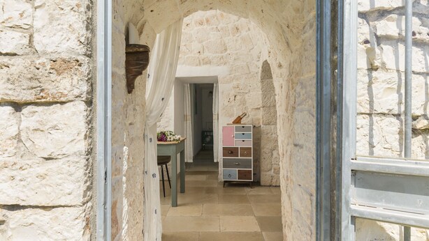 Un étroit couloir en pierre, avec une table en bois et un meuble aux couleurs vives.