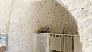 Une cuisine aux murs de pierre, équipée d’une cuisinière à gaz, d’un évier et d’un petit placard.
