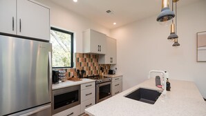 A modern kitchen with stainless steel appliances, white cabinetry, and a large window providing natural light. - Turf ROOFTOP + Sleeps Up to 16 If Renting Multiple Units! Unit B (Wilmington)