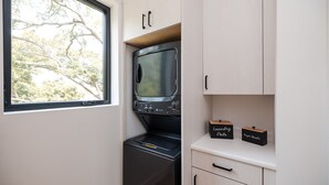 A compact kitchen with a microwave, a small refrigerator, and a window with a view of trees. There are two labeled storage boxes on the counter. - Turf ROOFTOP + Sleeps Up to 16 If Renting Multiple Units! Unit B (Wilmington)