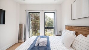 A modern bedroom with a large bed, a view of trees through the windows, and a mounted TV. - Turf ROOFTOP + Sleeps Up to 16 If Renting Multiple Units! Unit B (Wilmington)