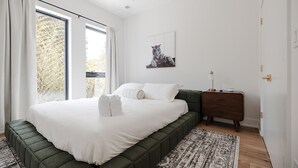 A bedroom with a large bed, a nightstand, a framed picture on the wall, and a window with curtains. - Turf ROOFTOP w Games and more in Heart of Wilmington! Rent Multiple or One Unit! Unit C (Wilmington)