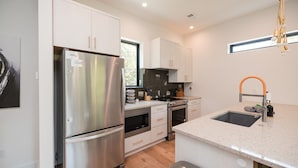 A modern kitchen with stainless steel appliances, white cabinetry, and a large window providing natural light. - Turf ROOFTOP w Games and more in Heart of Wilmington! Rent Multiple or One Unit! Unit C (Wilmington)